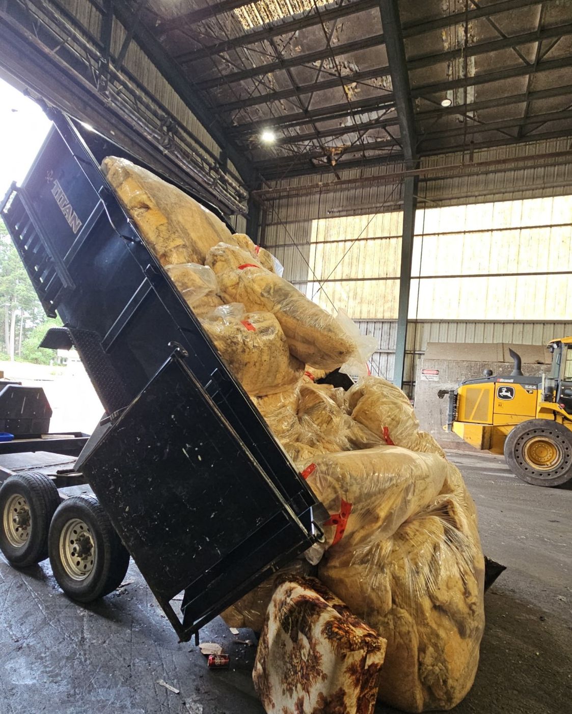 The Junk Matters trailer tipping bags of removed insulation inside a barn near Nanaimo