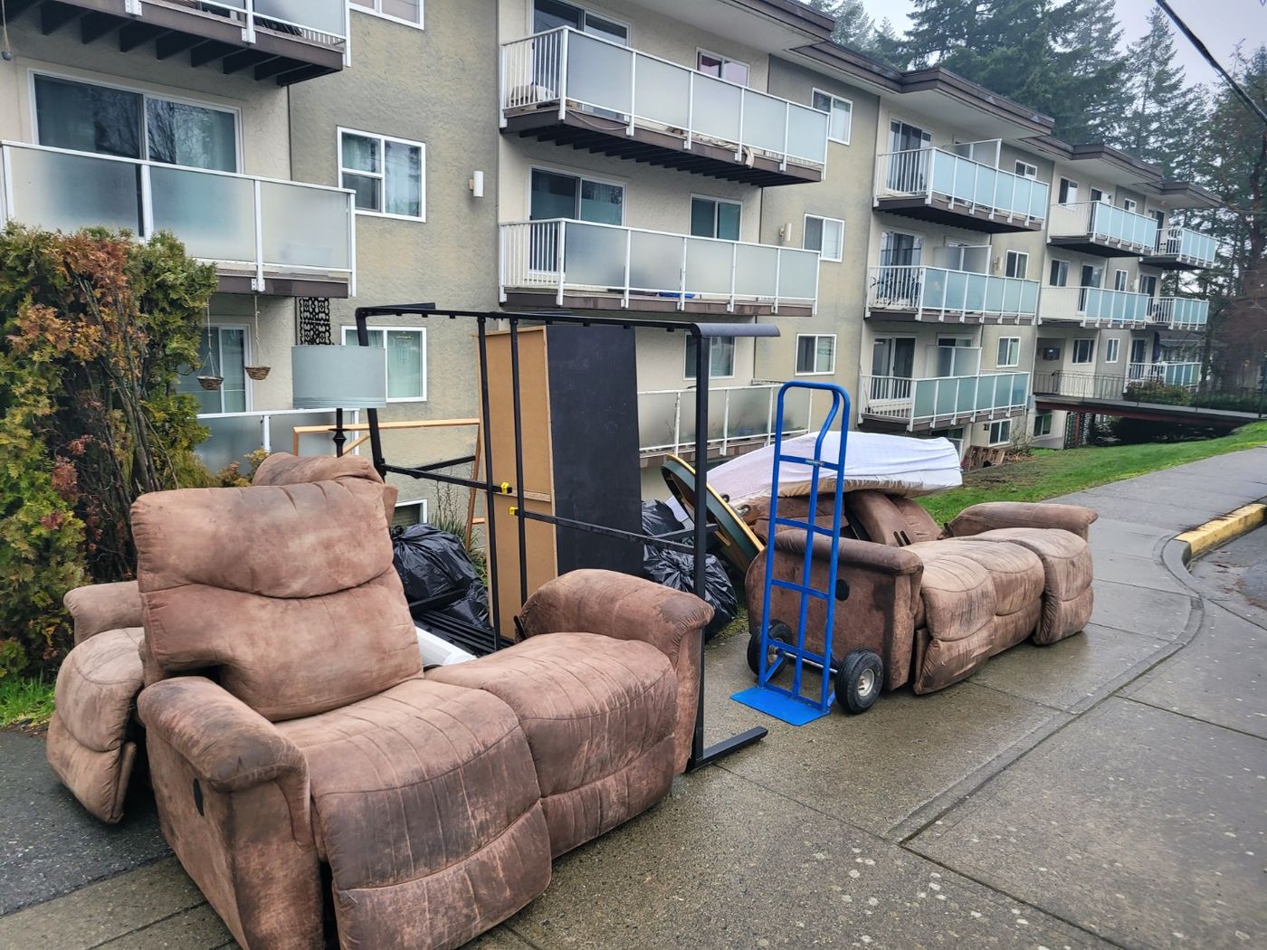 Two fabric recliners and a sofa set out on the sidewalk beside a Nanaimo apartment block, ready for Junk Matters to load