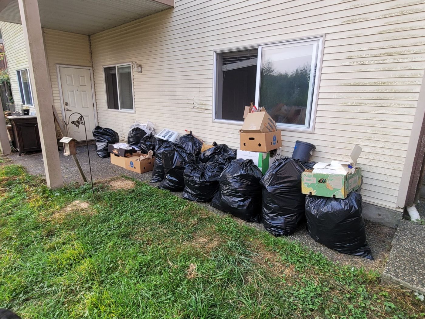 Black rubbish bags and boxes lined up along the side of a Nanaimo house awaiting pickup